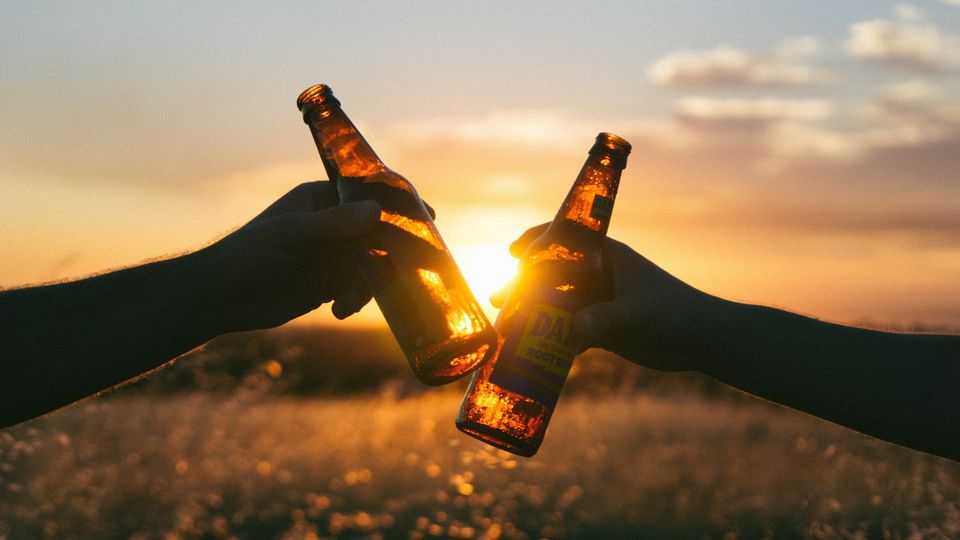 Two bottles clinking cheers with the sunset in the background.